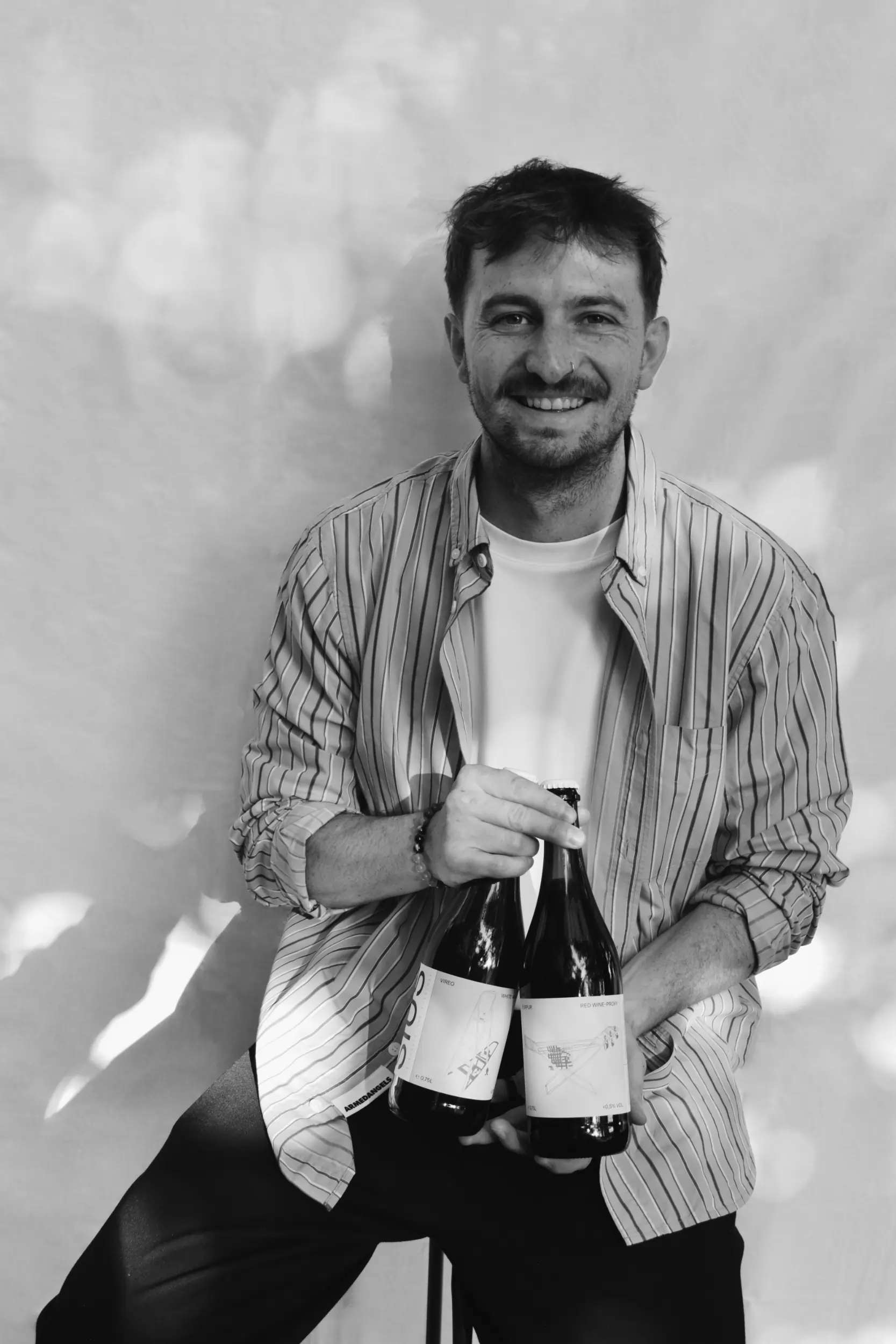 Der Gründer von SIUS Brewing sitzt in schwarz-weiß vor einem weißen Hintergrund und hält zwei Flaschen mit alkoholfreien Proxies in der Hand.