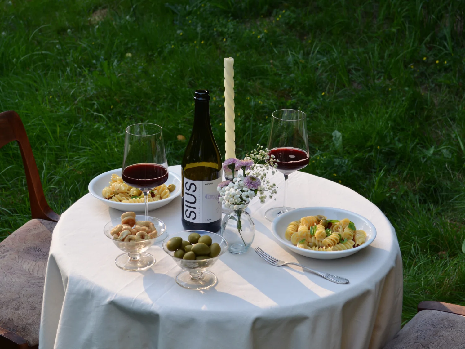 Ein Tisch mit kulinarischen Spezialitäten und einer Flasche SIUS PURPUR steht auf einer grünen Wiese.